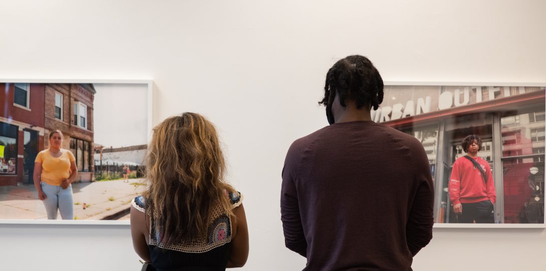 two gallery visitors with their backs to the camera looking at two photos