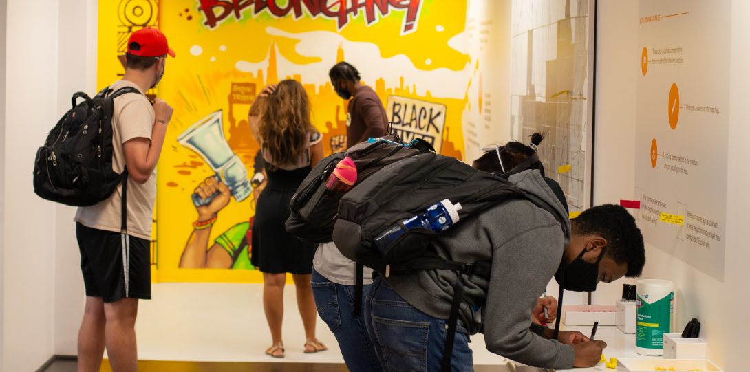 image of young men and women in a gallery hallways with a yellow mural at the end